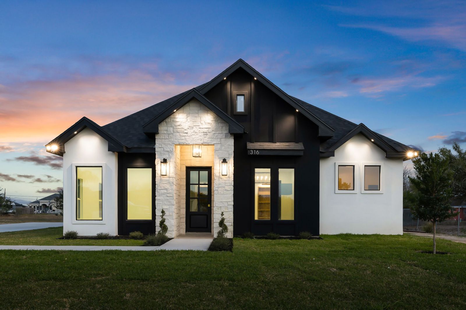 Dusk exterior with a white stone entry tower and black board-and-batten gable — The Black & Stone, a Kratos Construction custom home
