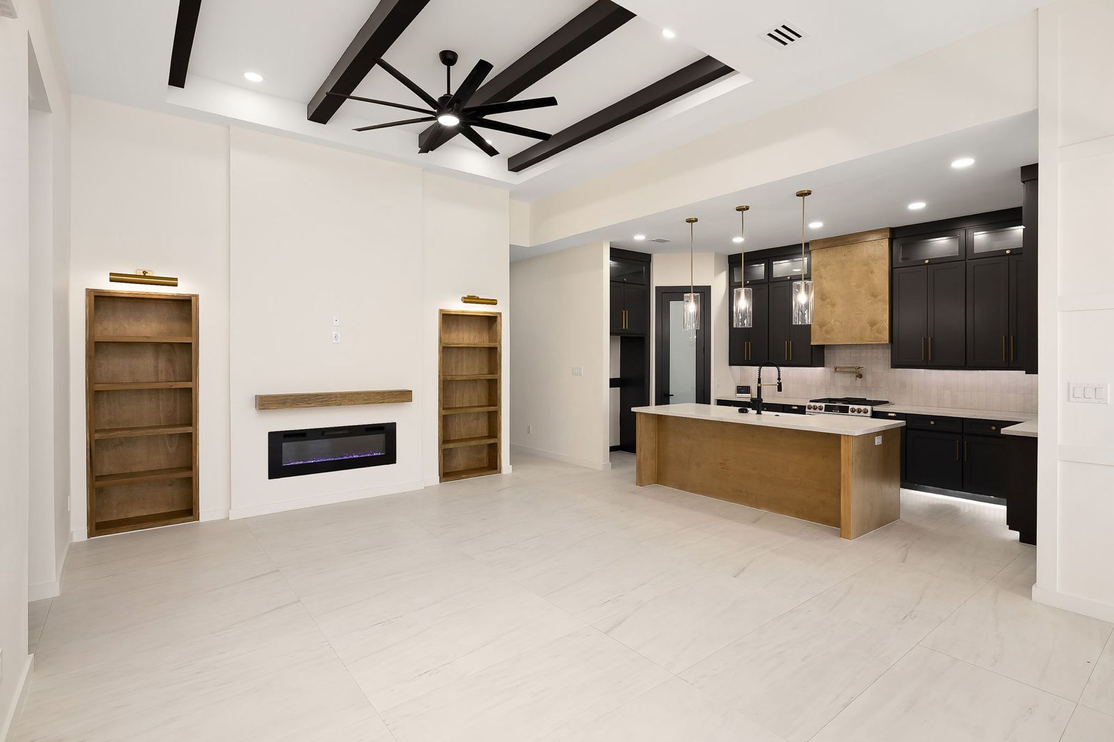 Great room with a dark beamed ceiling, linear fireplace and built-in shelving — The Black & Stone, a Kratos Construction custom home