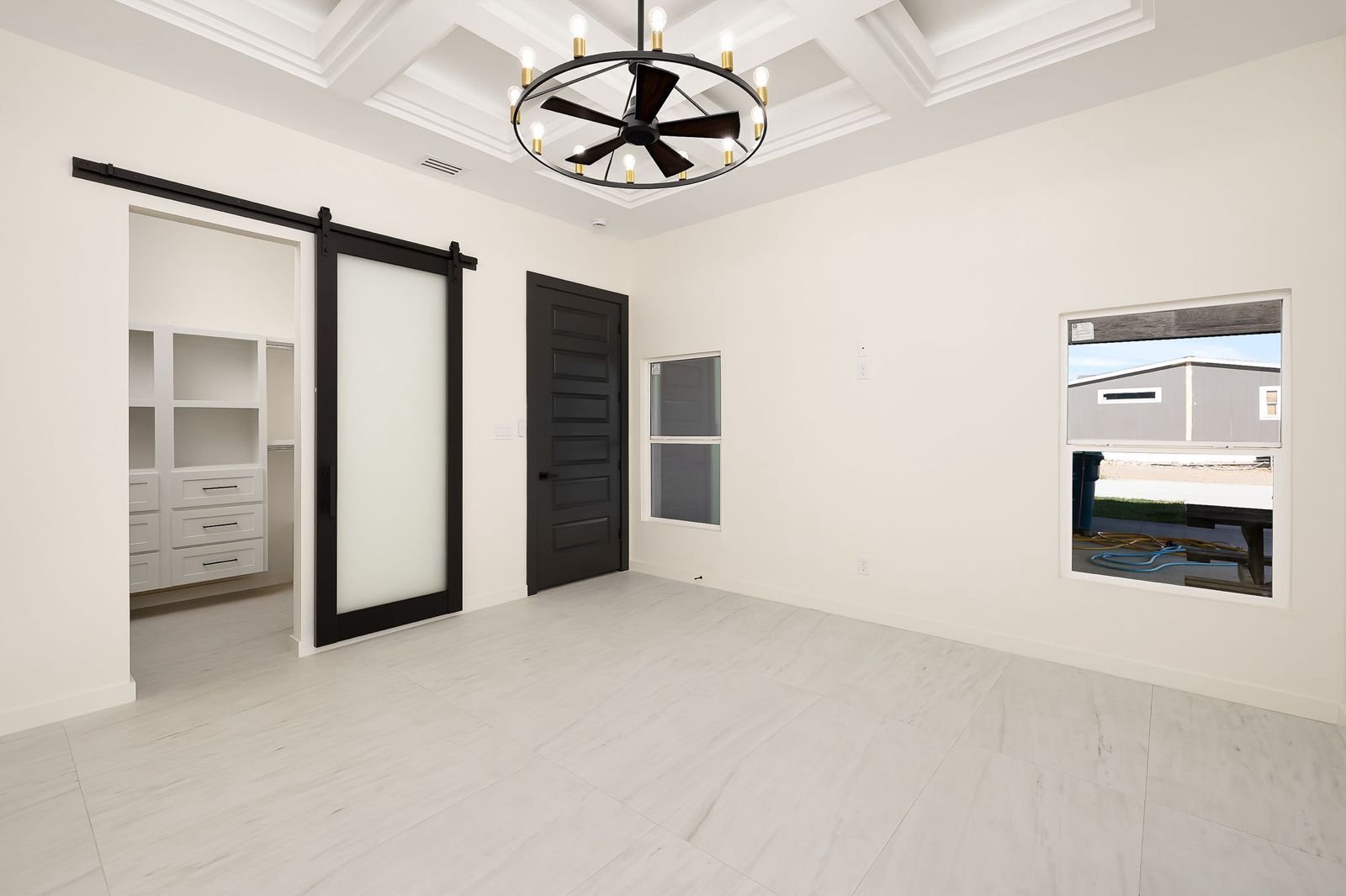 Primary bedroom with a coffered ceiling and black barn door — The Black & Stone, a Kratos Construction custom home