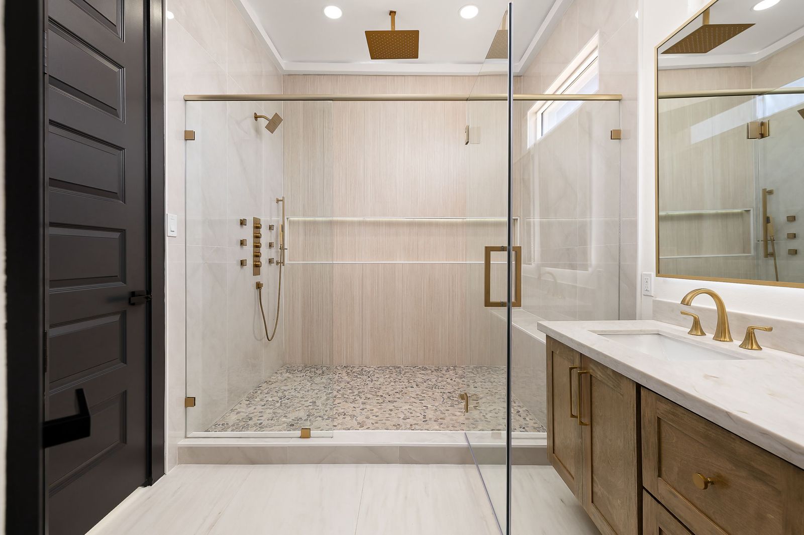 Walk-in shower with a rain head and brushed-gold fixtures — The Black & Stone, a Kratos Construction custom home