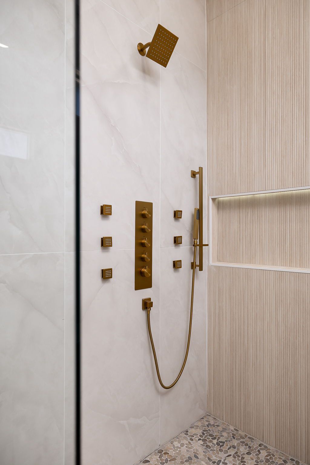 Shower with brushed-gold body sprays and a fluted tile accent wall — The Black & Stone, a Kratos Construction custom home