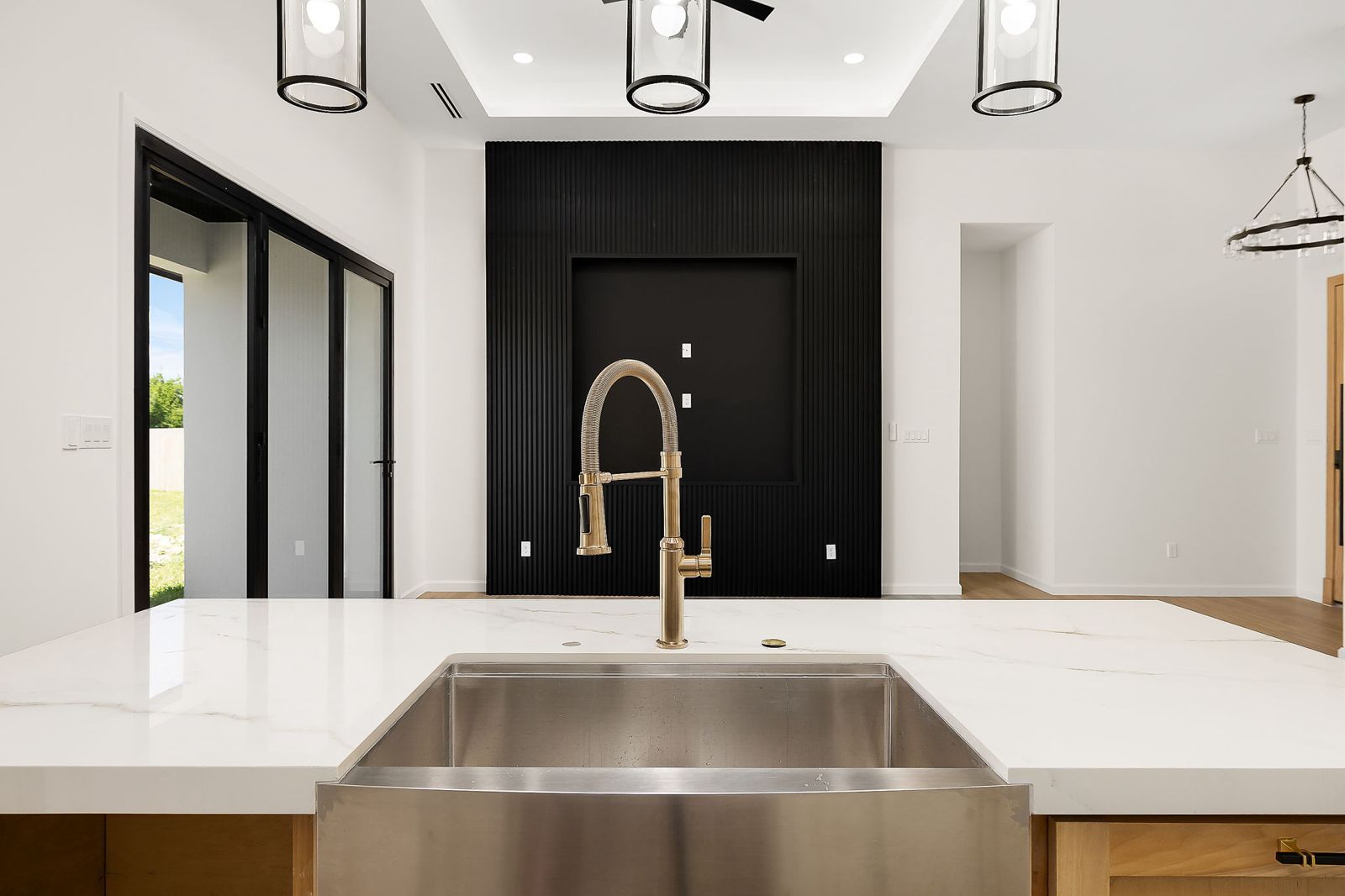Farmhouse sink with a brushed-gold faucet facing a black slat feature wall — The Modern Farmhouse, a Kratos Construction custom home