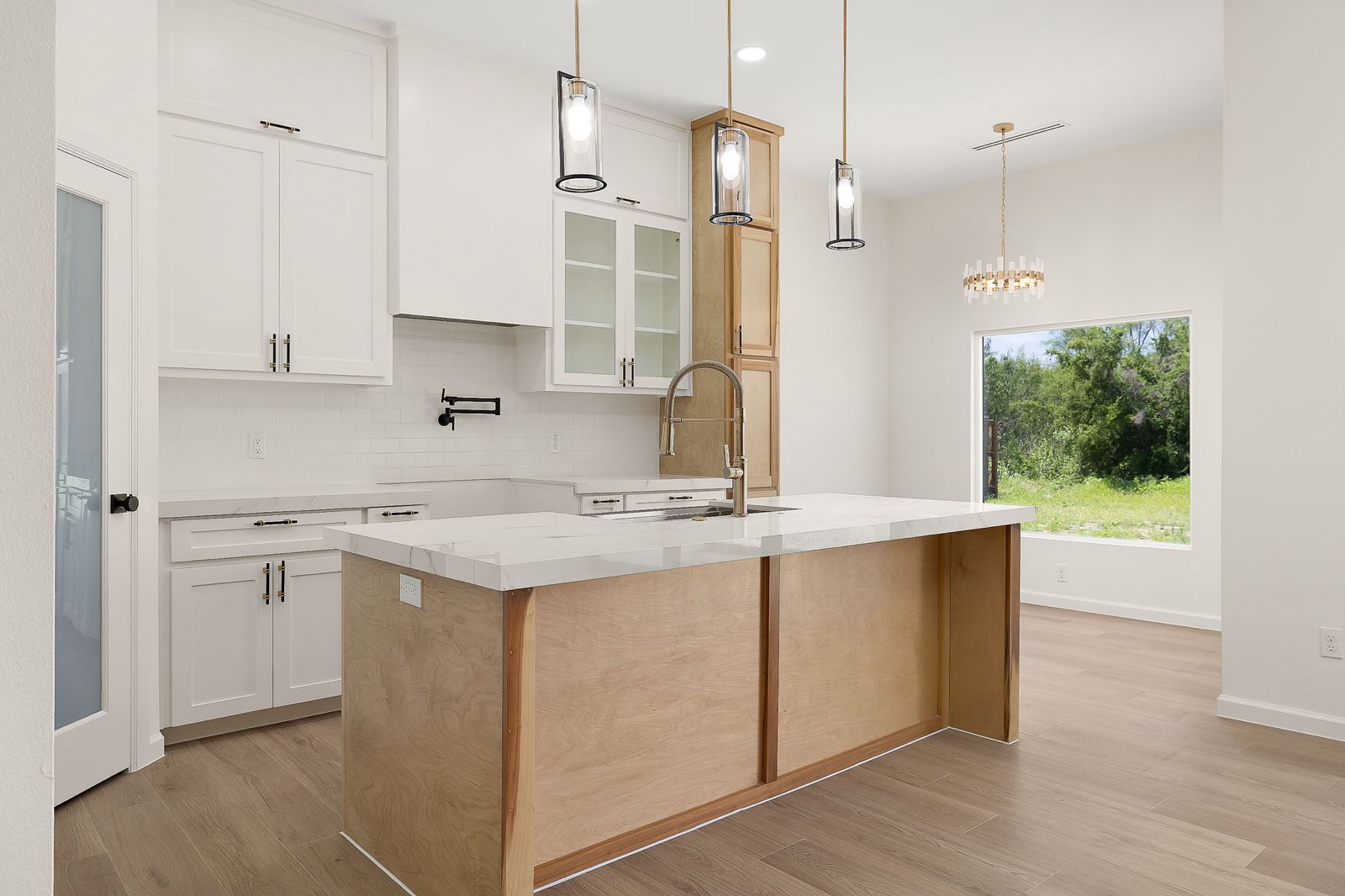 Kitchen island in natural oak with a picture window beyond — The Modern Farmhouse, a Kratos Construction custom home