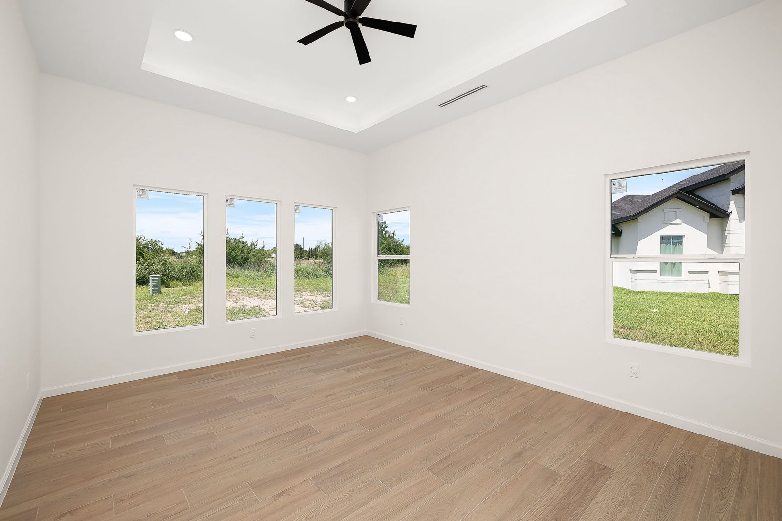 Bedroom with a tray ceiling and wood-look plank floors — The Modern Farmhouse, a Kratos Construction custom home