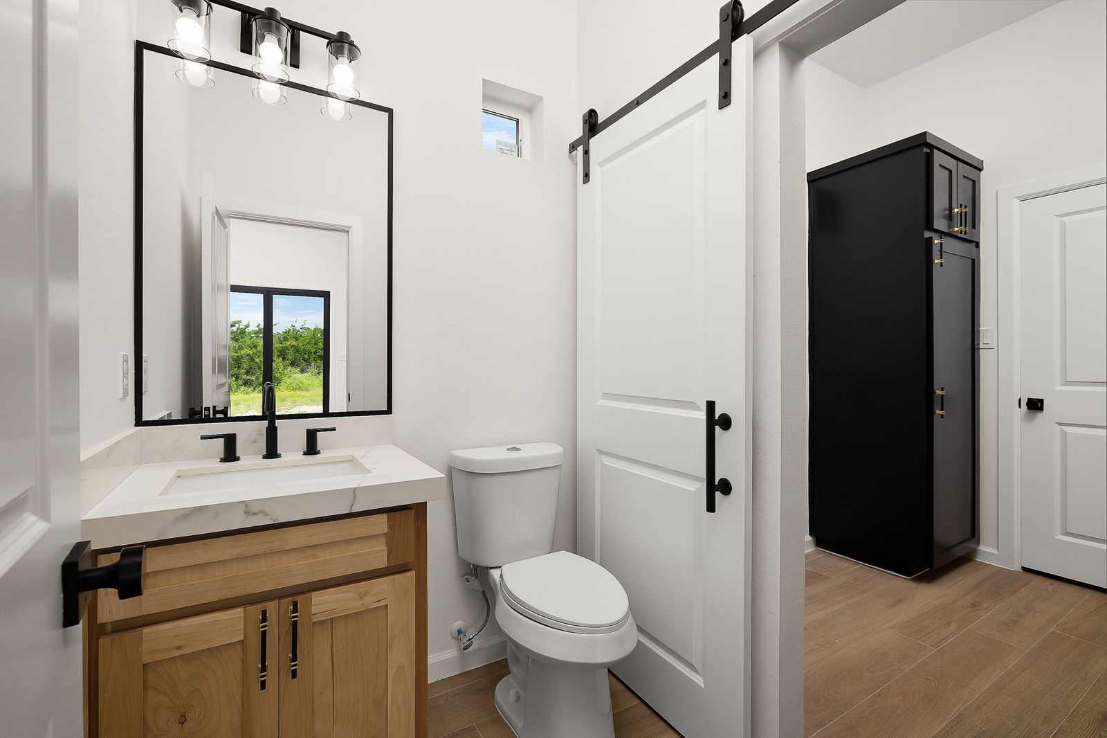 Half bath with an oak vanity and sliding barn door — The Modern Farmhouse, a Kratos Construction custom home