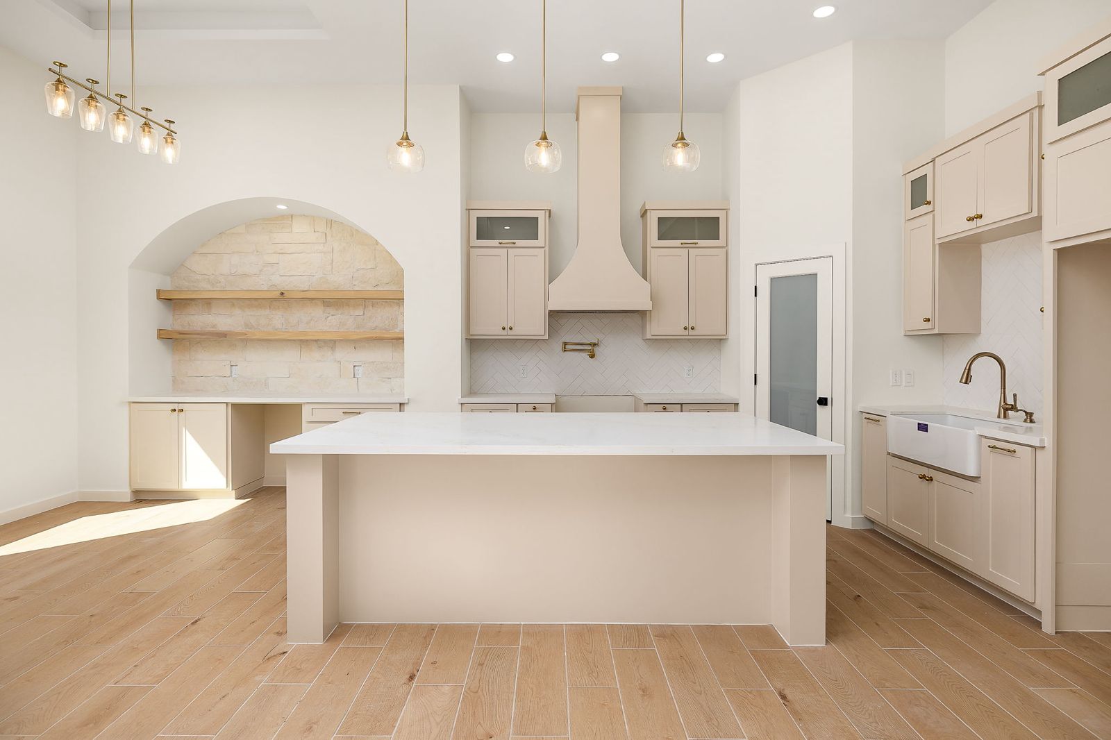 Kitchen with cream cabinetry, a plaster range hood and an arched stone niche — The Hill Country, a Kratos Construction custom home