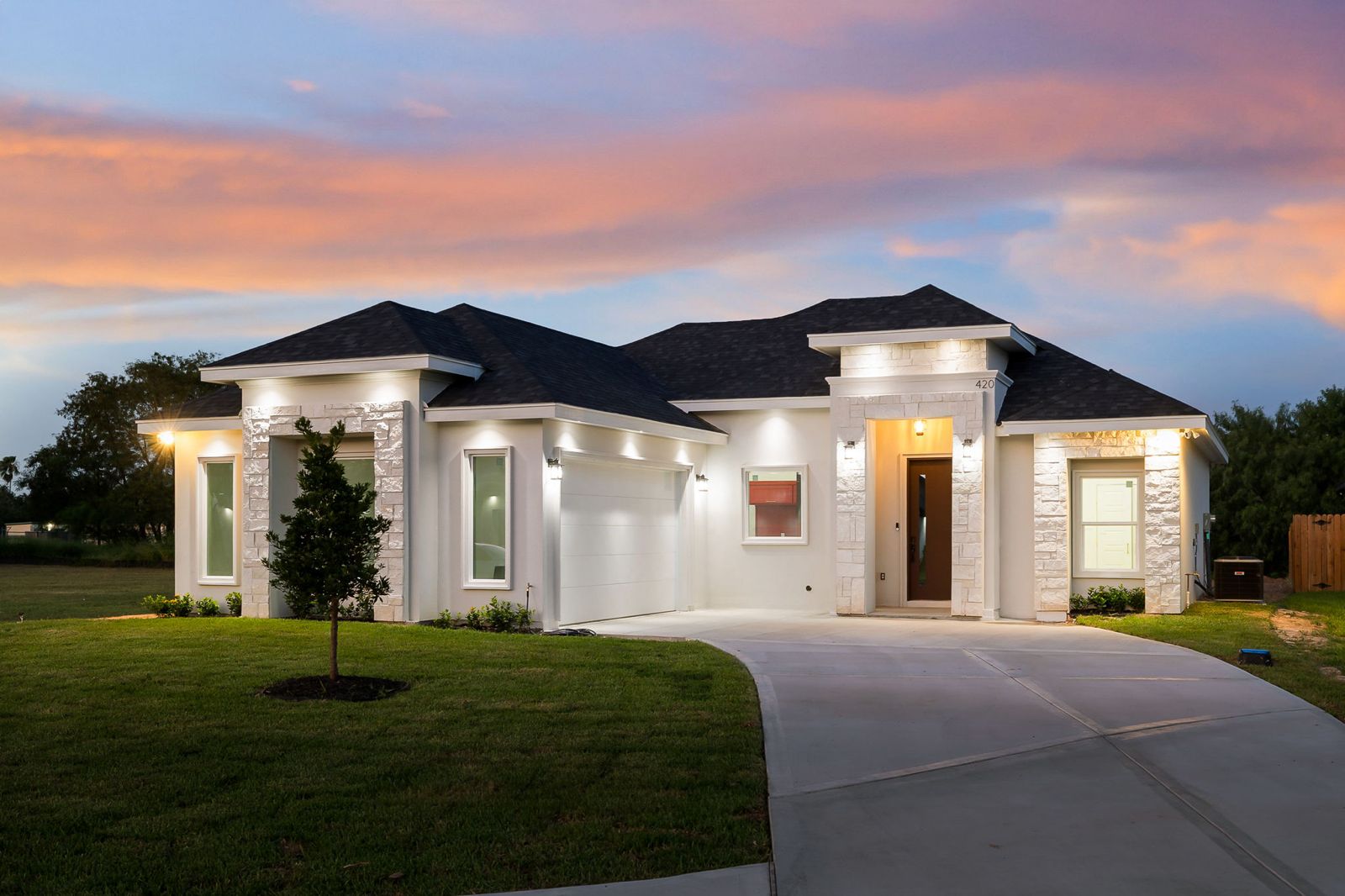 Dusk exterior with stone columns, stucco walls and a long driveway — The Stone Column, a Kratos Construction custom home