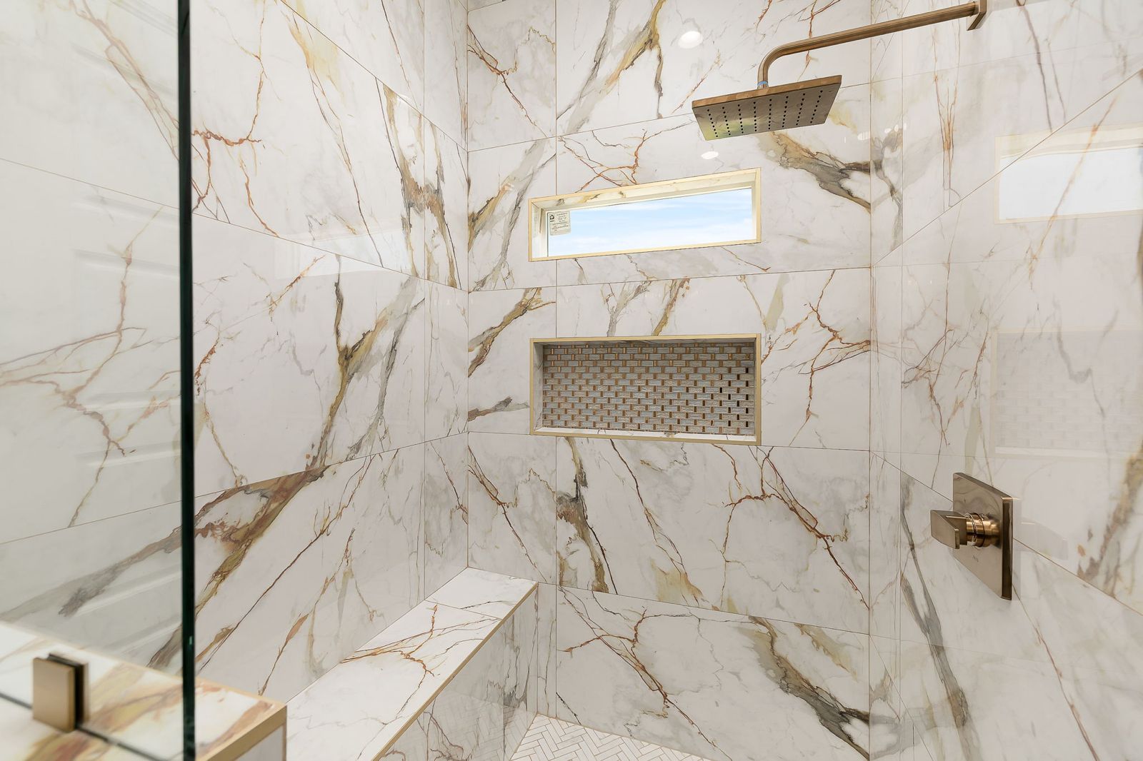 Walk-in shower in gold-veined marble tile with a bench and niche — The Stone Column, a Kratos Construction custom home