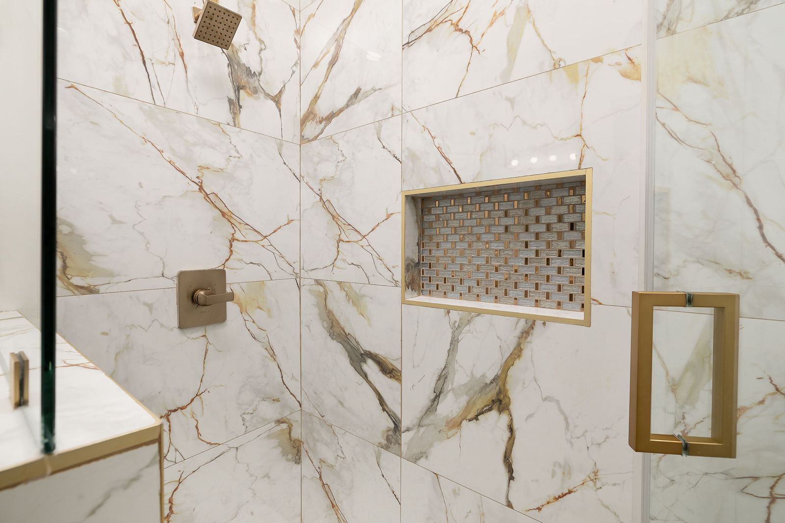 Shower niche and brushed-gold fixtures in gold-veined marble — The Stone Column, a Kratos Construction custom home
