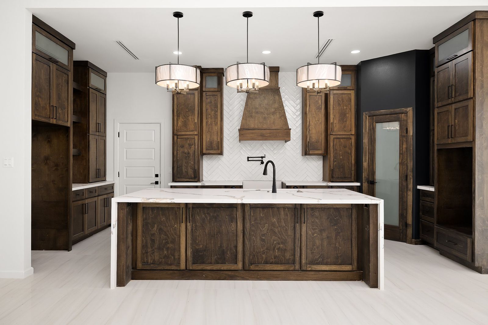 Kitchen with stained-wood cabinetry, a quartz waterfall island and drum pendant lights — The Stone & Timber, a Kratos Construction custom home