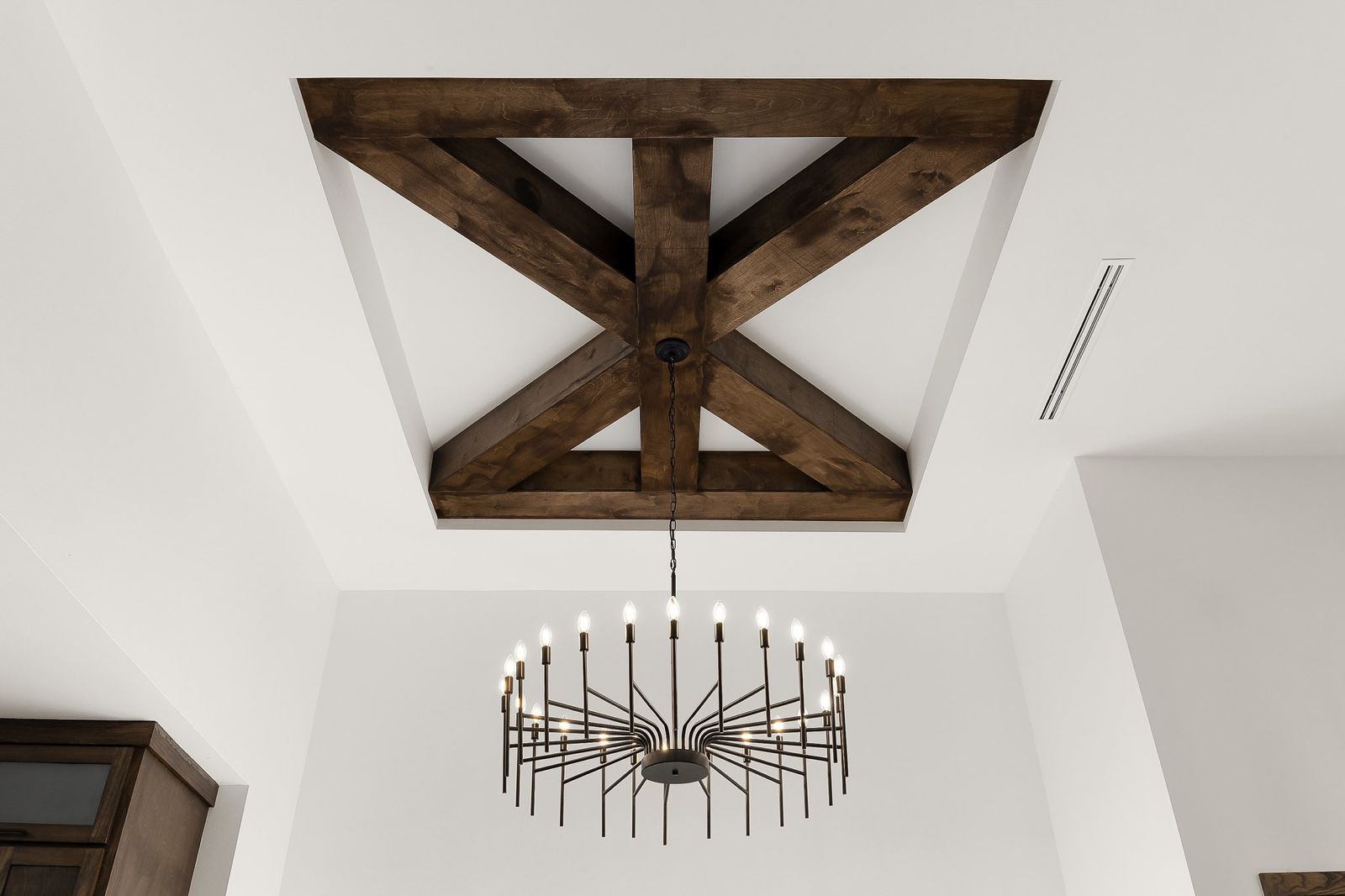 Exposed timber beam ceiling detail with a candle-style chandelier — The Stone & Timber, a Kratos Construction custom home