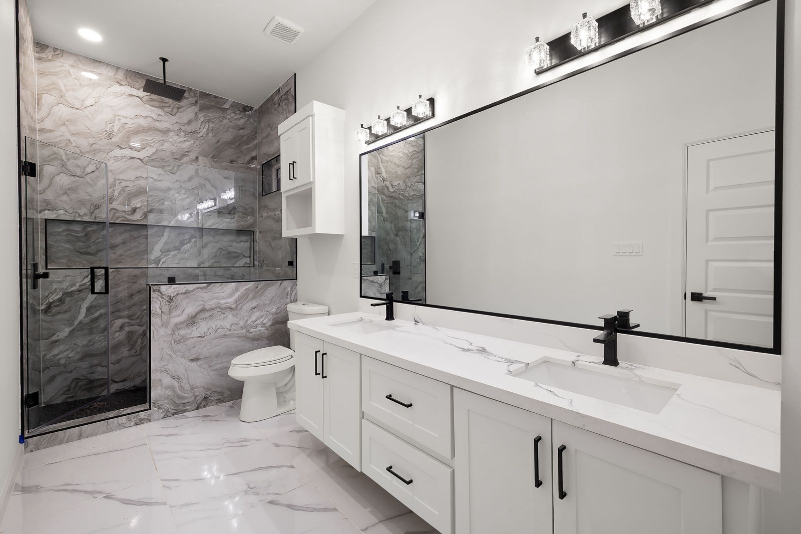 Primary bathroom with a stone-look walk-in shower and long double vanity — The Timber Gable, a Kratos Construction custom home